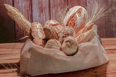 Different types of seed bread in a raffia sack on a wooden table with ears of wheat