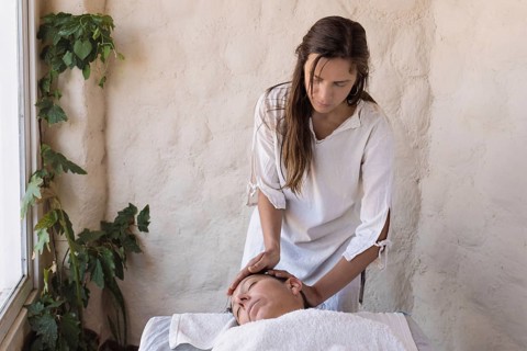 Beautiful young therapist performing massage in spa salon. Front view portrait of beautician doing facial massage to relaxed female client. Facial beauty treatment