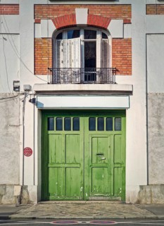 Town building facade with a green garage gate and window with louvers above the door