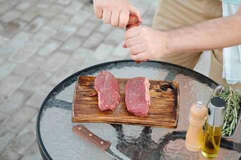 Top view of unrecognizable man seasoning raw beef steak with pepper preparing meal for grill