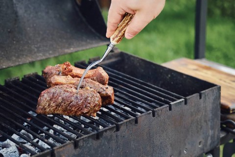 Unrecognizable man grilling steak outdoors. He turns meat with fork