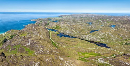Aerial panorama of the sparsely populated North West Highlands with the single track road and pass road B869 running along the freshwater loch at Ordain. On the horizon the Atlantic Ocean