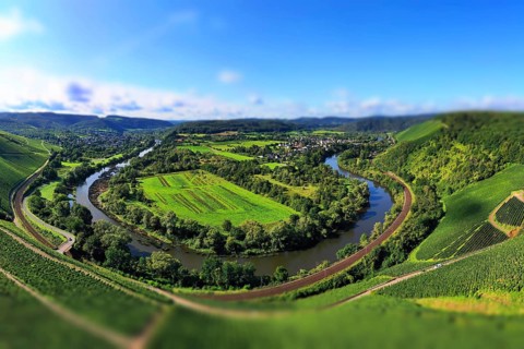 Wiltinger Saarbogen. The river winds through the valley and is surrounded by vineyards and green forests. Kanzem