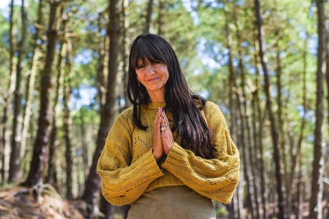 Smiling woman clasping hands while looking at camera outdoors