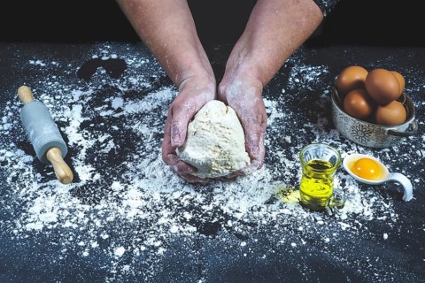 Woman with bread dough in her hands on a black table with flour