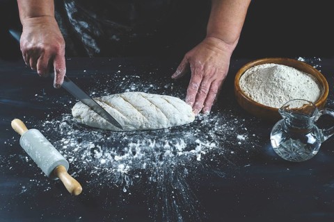 Woman cutting with a knife a flour dough to make homemade bread on a black wooden table with flour
