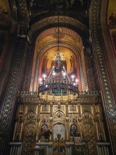 Interior details of Curtea de Arges monastery. The altar and ornate walls with painted icons and a golden chandelier with lights suspending out of ceiling