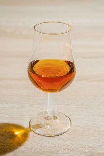 Tulip glass with cognac on wooden table under hard sunlight