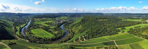 Wiltinger Saarbogen. The river winds through the valley and is surrounded by vineyards and green forests. Kanzem