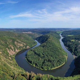 Aerial view of the Saar Loop. The Saar winds through the valley and is surrounded by green forests. Orscholz