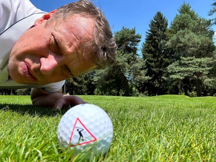Golfer Looking at a Golf Ball with Warning Sign on the Fairway in a Sunny Day in Switzerland