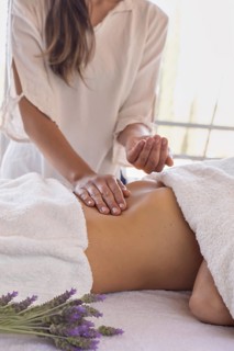 Woman masseuse with patient on massage table placing oil on her abdomen