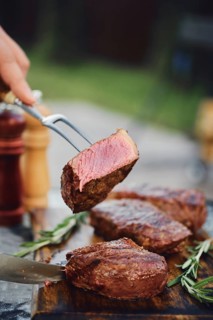 Unrecognizable man holds piece of grilled strip steak on the fork