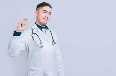 Friendly doctor holding a syringe isolated. Smiling doctor showing a syringe on isolated background. Doctor and vaccine concept