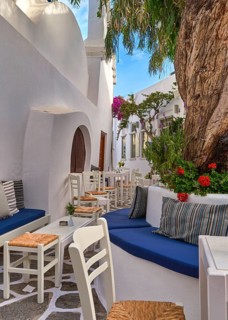 Beautiful outdoor cafe or bar in narrow streets of Greek town on sunny summer day offers refreshing shade under trees