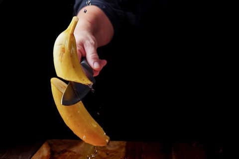 Woman cutting a banana in half with a knife in the air spilling water