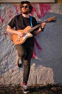 Hipster street musician in black playing electric guitar in the street on sunset leaning on a wall. Lisbon