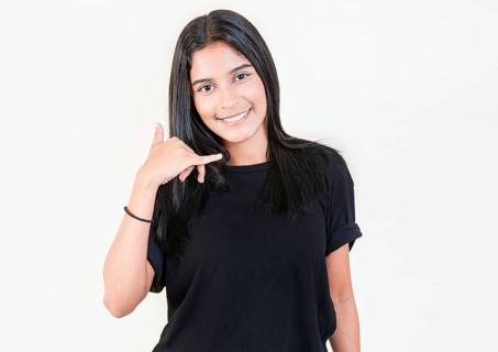 Smiling young girl gesturing call me with hand isolated. Happy latin girl gesturing call with fingers isolated