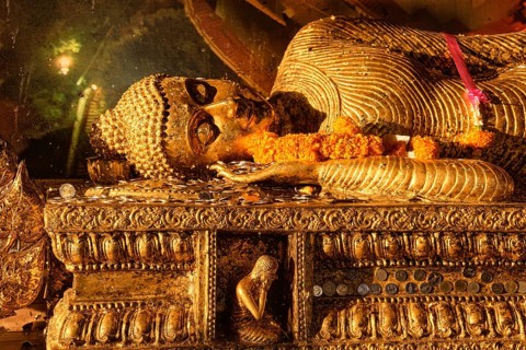 Statue of reclining Buddha covered with golden leaves