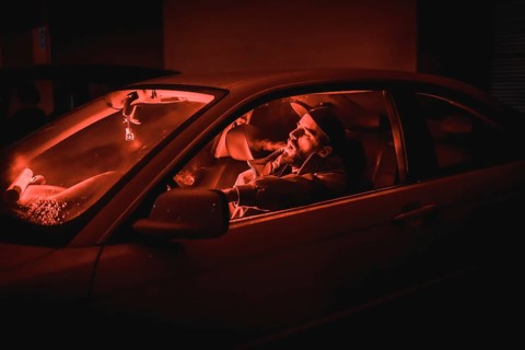 Rapper man in a cap in a car smoking at night in a garage lit with a red light in winter