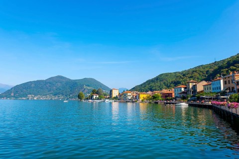 City of Porto Ceresio on Waterfront with Mountain and Lake Lugano in a Sunny Summer Day in Porto Ceresio