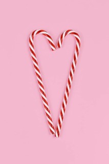 Christmas candy canes forming shape of heart on pink background