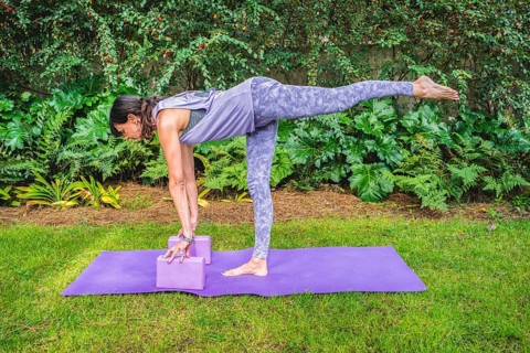 Fit woman in sportswear practices yoga pose using a block outdoors. Yoga with brick