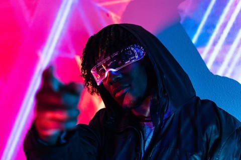 Studio portrait with purple and blue neon lights of a futuristic man pointing ahead wearing artificial intelligence goggles