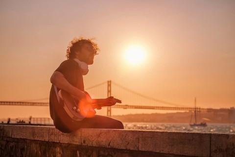 Hipster street musician in black playing electric guitar in the street on sunset