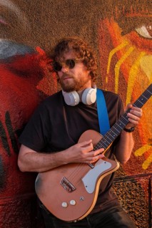 Hipster street musician in black playing electric guitar in the street on sunset leaning on a painted wall