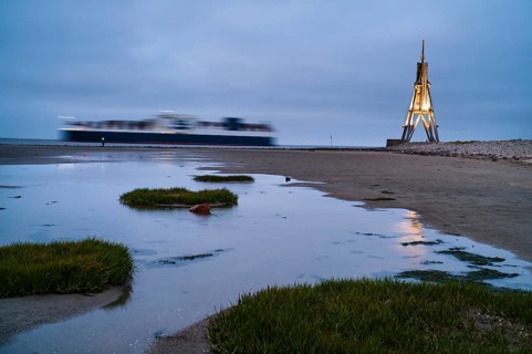 Kugelbake illuminated with cargo ship at dusk