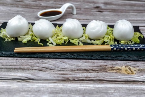 Xiao long bao of prawns on a bed of lettuce on a slate plate with chopsticks and a ceramic spoon with soy sauce