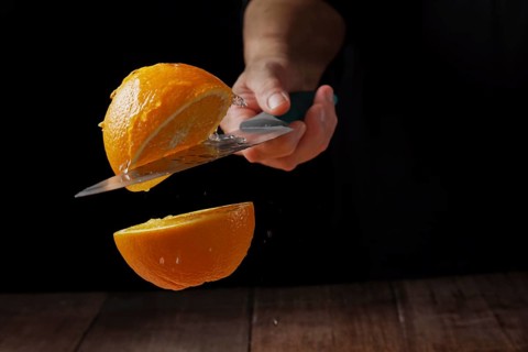 Woman cutting an orange in half with a knife in the air spilling water