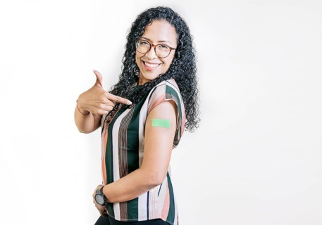 Smiling woman pointing at her vaccinated arm. Latin woman pointing at the bandage on her vaccinated arm