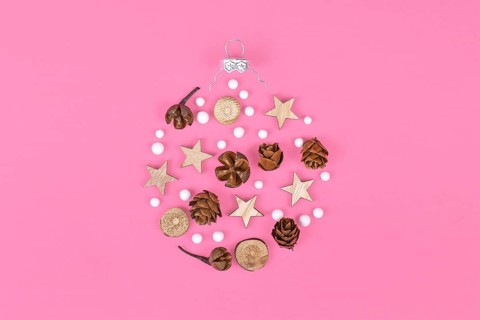 Seasonal ornaments like natural hernlock cones and stick slices with stars and white snowballs forming shape of Christmas tree bauble on pink background