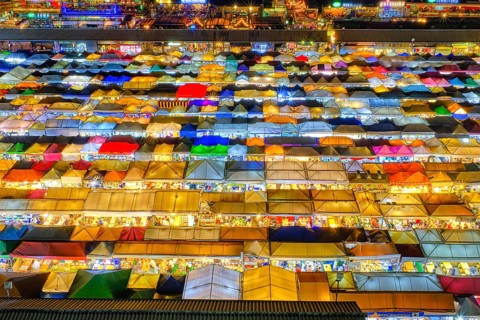 Close-up view of rows of colorful outdoor market tents and food stalls at night. Fairs