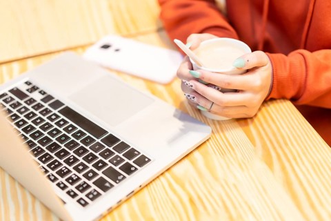 Alternative unrecognizable person with a hot coffee surfing the internet on the computer