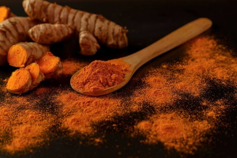 Fresh turmeric root and ground turmeric in a wooden spoon isolated on black background and copy space