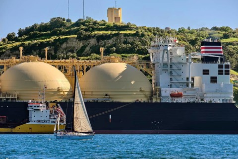 LNG or liquified natural gas tanker moored by industrial pier and green hill on sunny day. Alternative gas supply