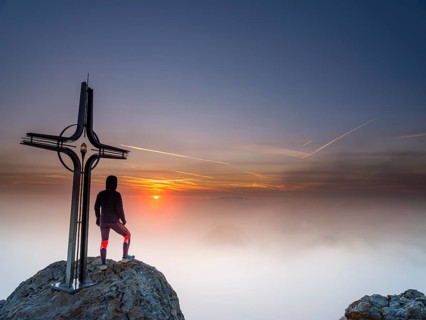 Mountaineer at the summit cross Hohe Goell at sunrise