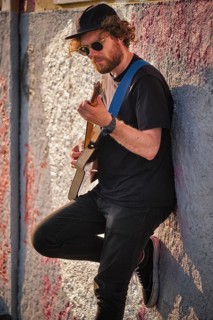 Hipster street musician in black playing electric guitar in the street on sunset leaning on a wall. Lisbon