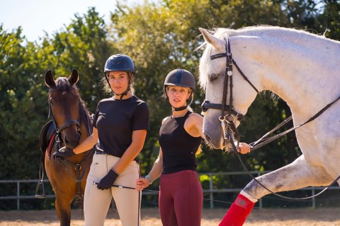 Two young Caucasian girl riders smiling next to their white and brown horses on a horse