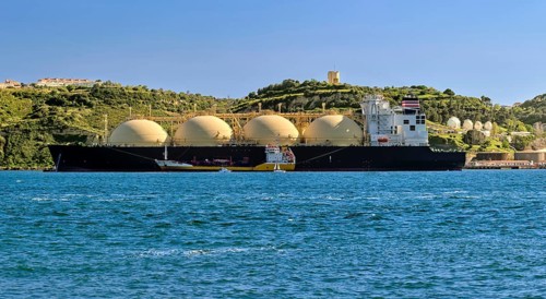 LNG or liquified natural gas tanker moored by industrial pier and green hill on sunny day. Alternative gas supply