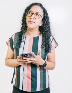 Thoughtful young woman in glasses holding cell phone isolated. Pensive latin girl holding smart phone isolated