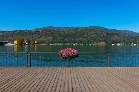 Elevated Walkway with Flowers on the Railing on Lake Lugano with Mountain in a Sunny Summer Day in Porto Ceresio