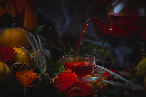 Pouring tea into glass cup surrounded by Halloween decorations