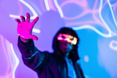 Studio portrait with purple and blue neon lights with focus on the hand of a futuristic man with AR goggles