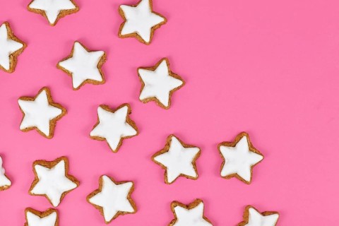 German star shaped glazed cinnamon Christmas cookies called 'Zimtsterne' on pink background