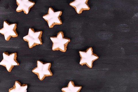 German star shaped glazed cinnamon Christmas cookies called 'Zimtsterne' on dark black background