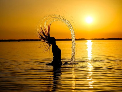Young woman in the water throws back her long hair with a surge of water